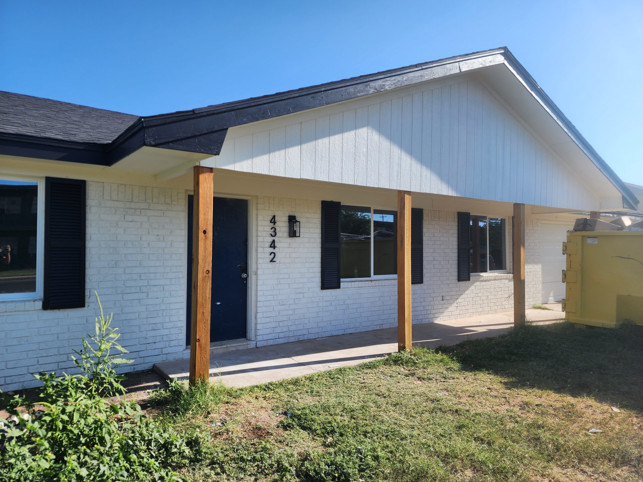 Exterior home renovation in Austin TX by Cuatro Pilares featuring painted brick, new wood porch posts, black trim, and updated front entry design