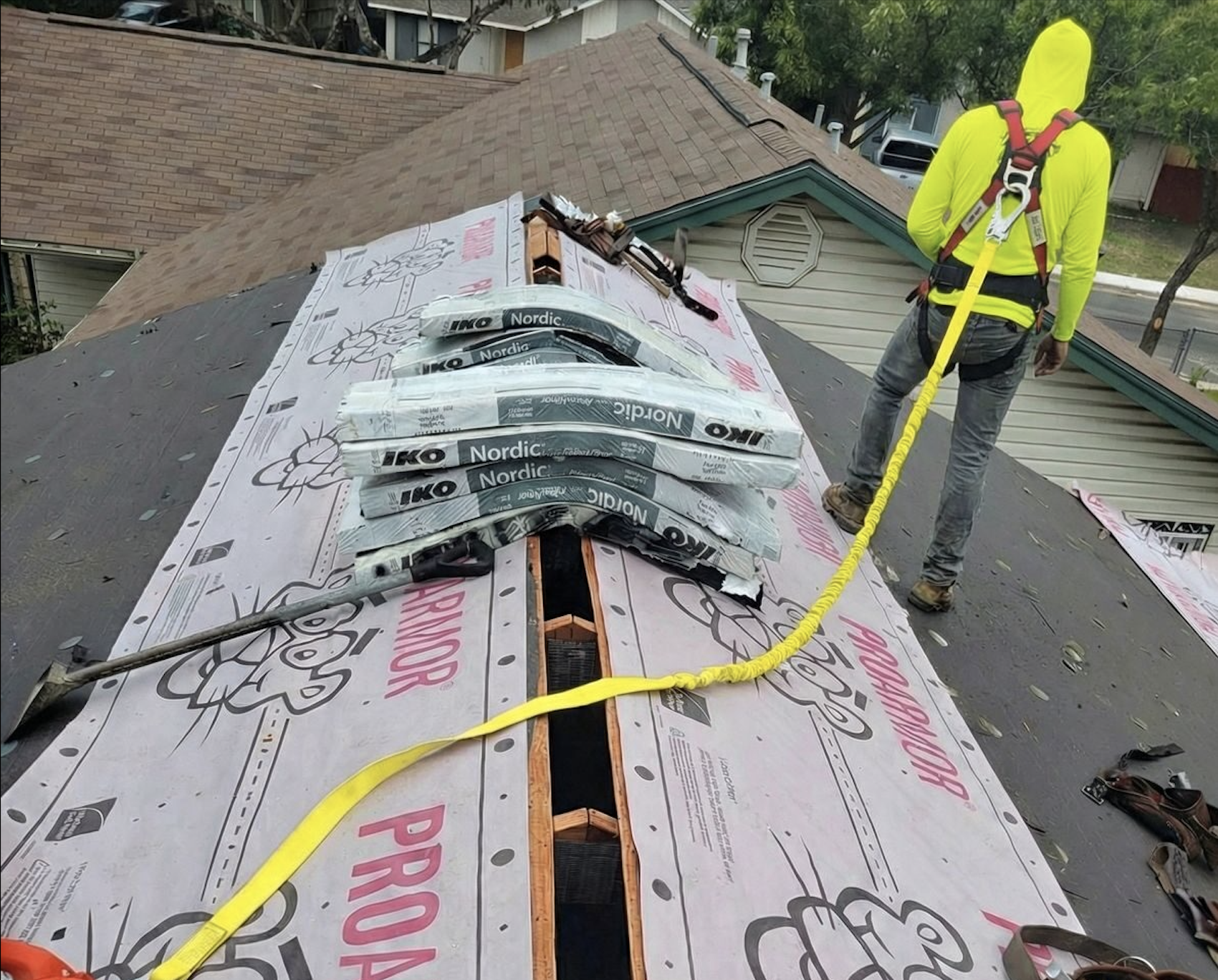 Roofing contractor installing ridge vent system on residential roof with synthetic underlayment and safety harness