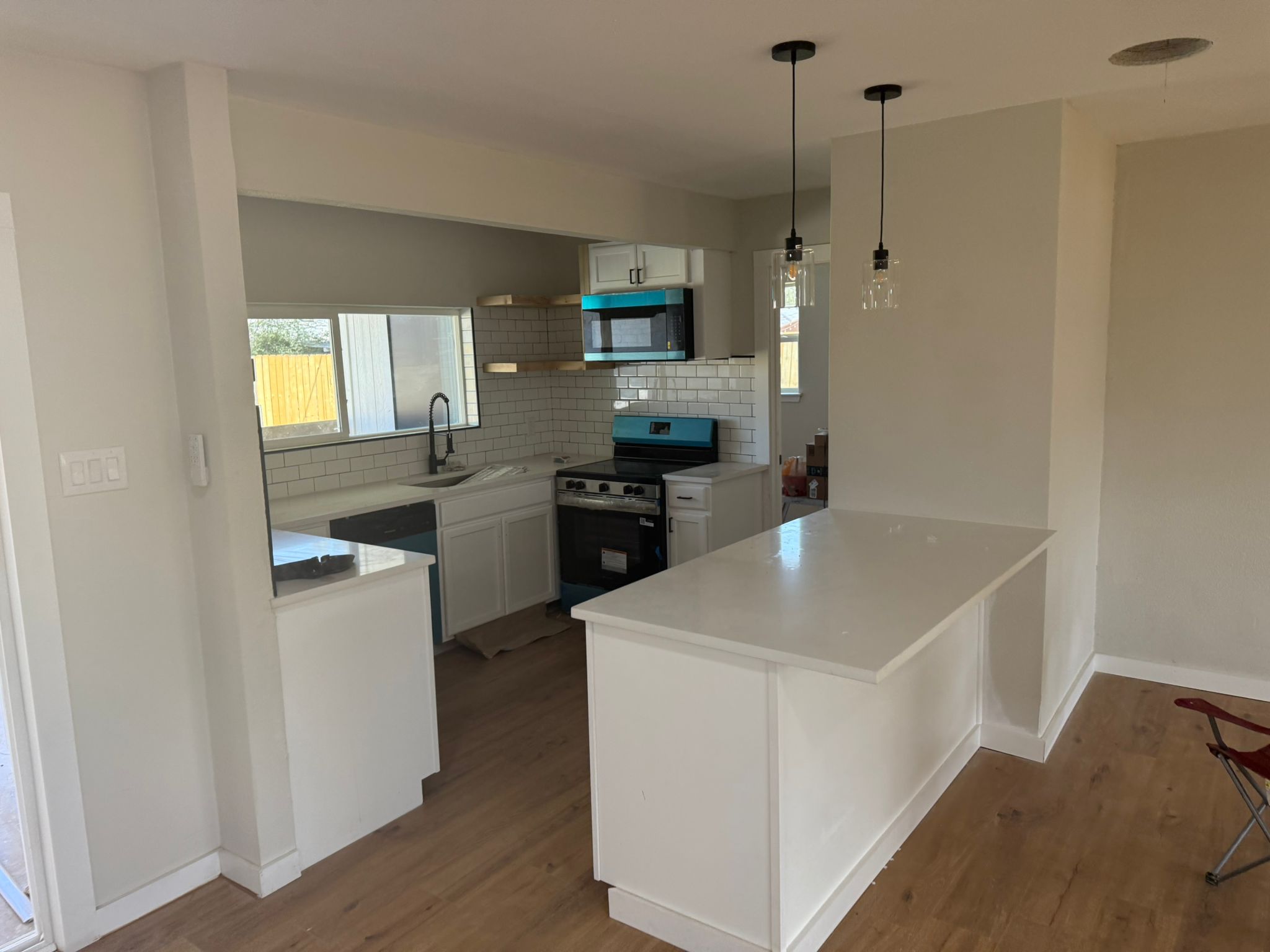 Open concept kitchen remodel in Austin TX by Cuatro Pilares featuring white cabinets, center island, subway tile backsplash, and modern lighting fixtures
